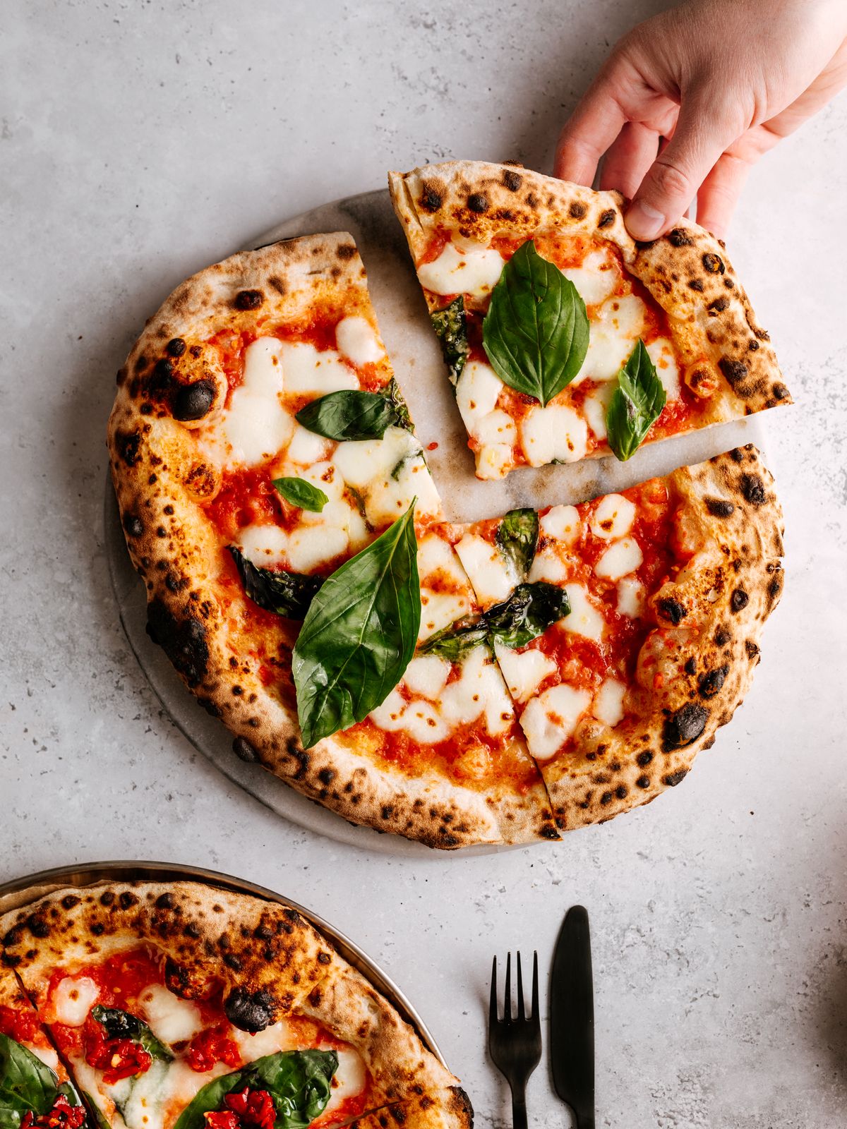 Saftige Pizza Margherita mit Mozzarella und Basilikum, eine Hand nimmt ein Stück